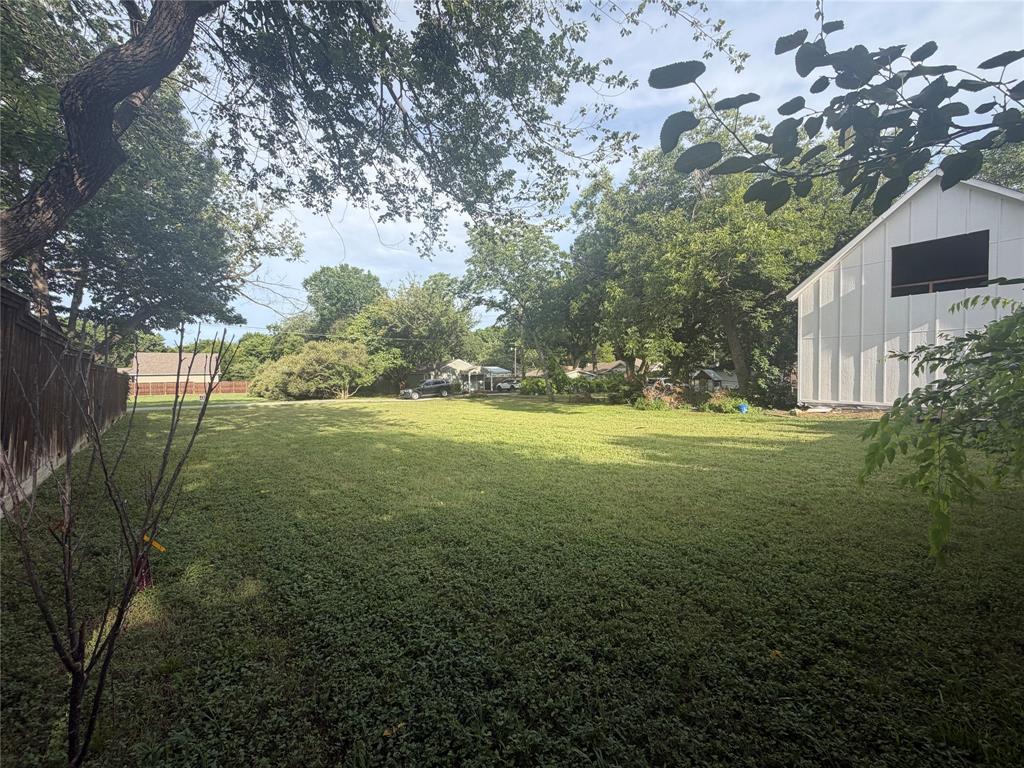 Expansive lot featuring mature trees, a wood-slat perimeter fence, and a white board-and-batten exterior structure