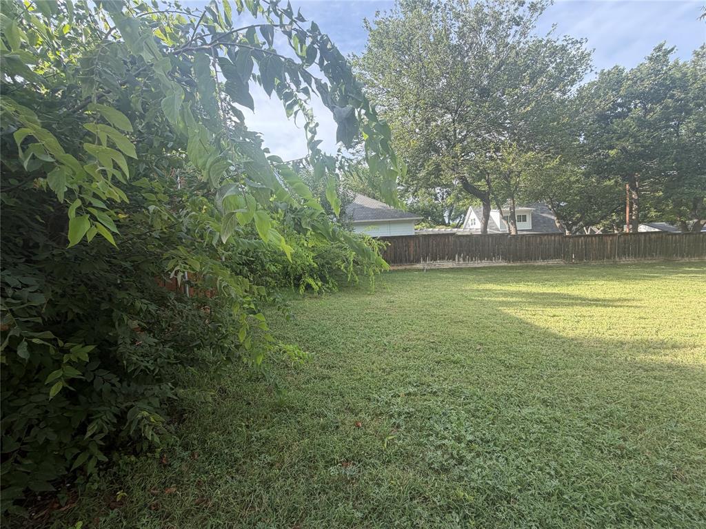 Expansive backyard featuring a grass lawn, mature trees, and perimeter wood fencing