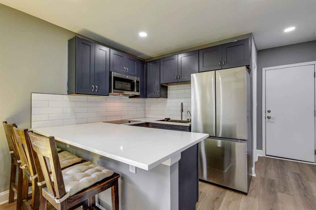 Kitchen featuring dark shaker-style cabinetry, quartz countertops with an extended breakfast bar, white subway tile backsplash, stainless steel appliances, and wood-finish flooring
