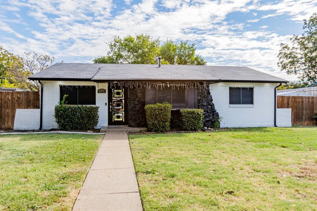 Single-story exterior featuring painted white brick, decorative stone masonry accents, a concrete walkway, and wood-panel privacy fencing