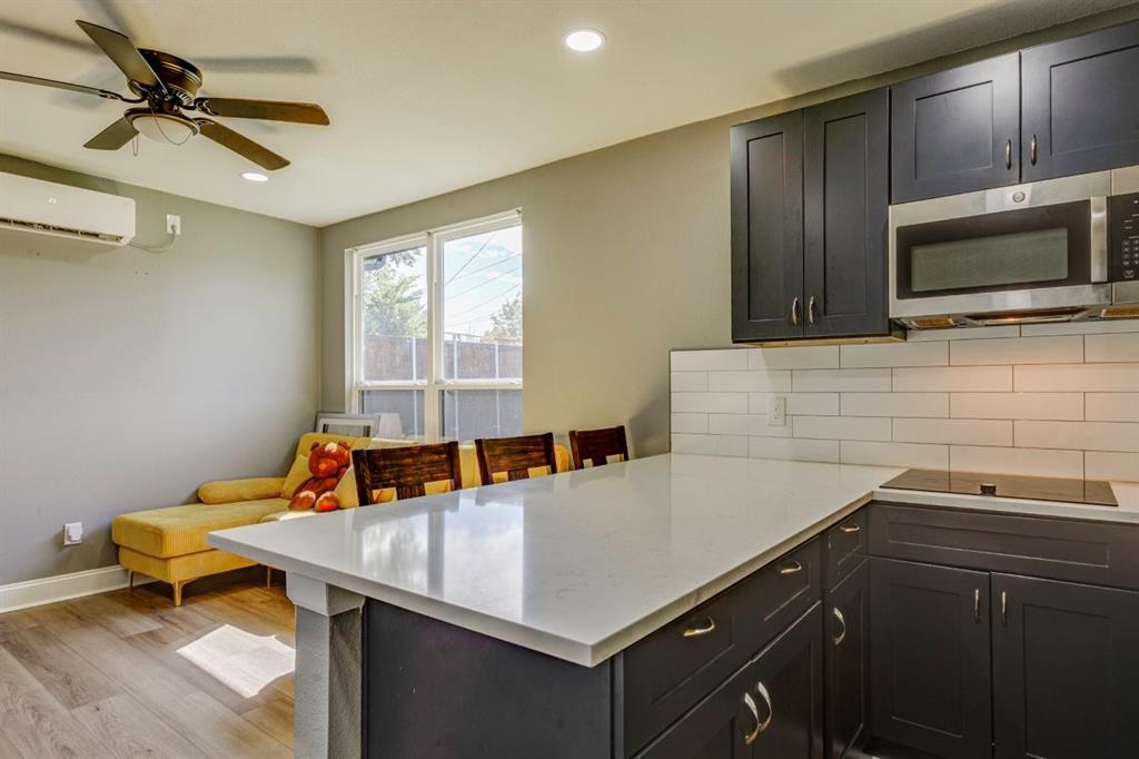 Kitchen featuring dark-finish cabinetry, quartz countertops, white subway tile backsplash, stainless steel microwave, and wood-finish flooring