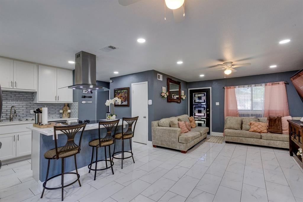 Open-concept kitchen and living area featuring white cabinetry, a stainless steel chimney-style range hood, recessed lighting, and tile flooring