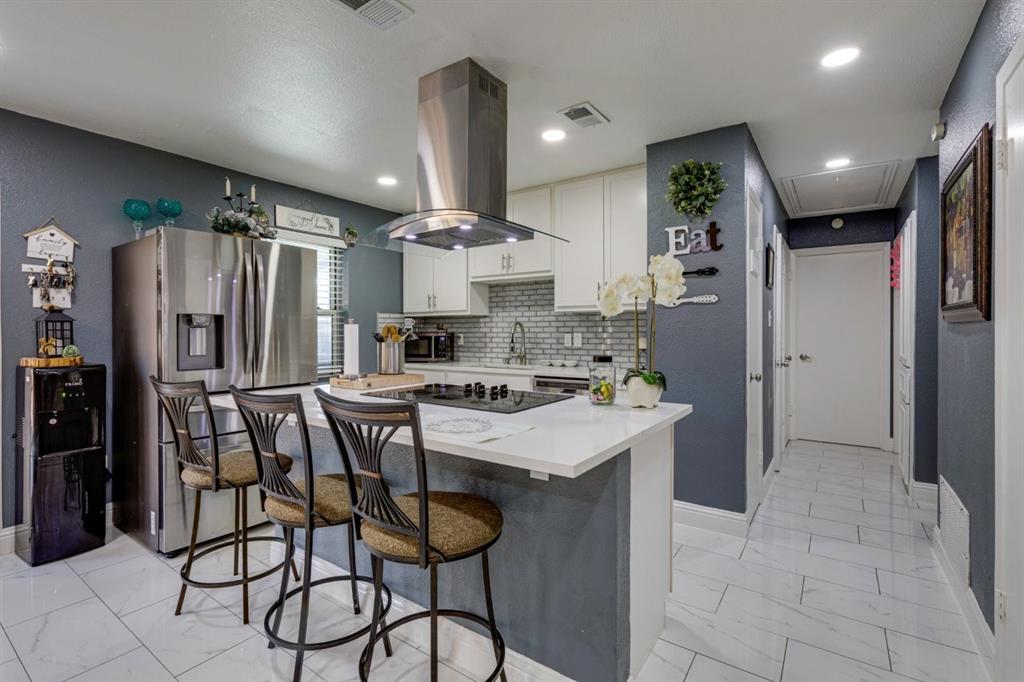 Kitchen featuring white cabinetry, solid-surface countertops, stainless steel appliances, a center island with a built-in cooktop and stainless steel range hood, and tile flooring