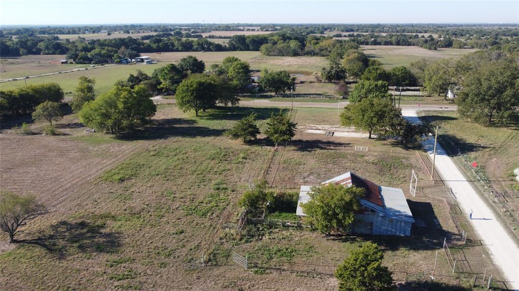 Expansive acreage featuring mature trees, a metal-roof structure, wire fencing, and gravel road access