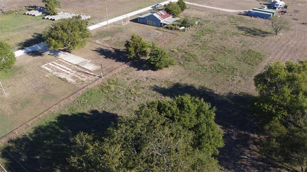 Expansive acreage featuring mature trees, a metal-roof structure, wire fencing, and gravel road access