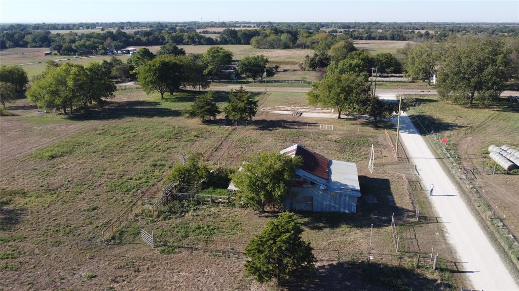 Expansive acreage featuring mature trees, a metal-roof structure, gravel road frontage, and fenced enclosures