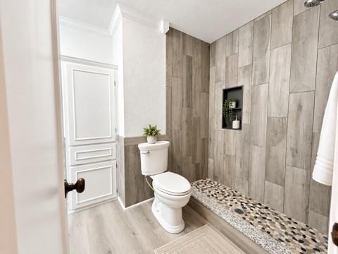 Walk-in shower featuring vertical wood-finish wall tile, a built-in recessed niche, and a stone-tiled floor, complemented by wood-finish flooring and paneled cabinetry