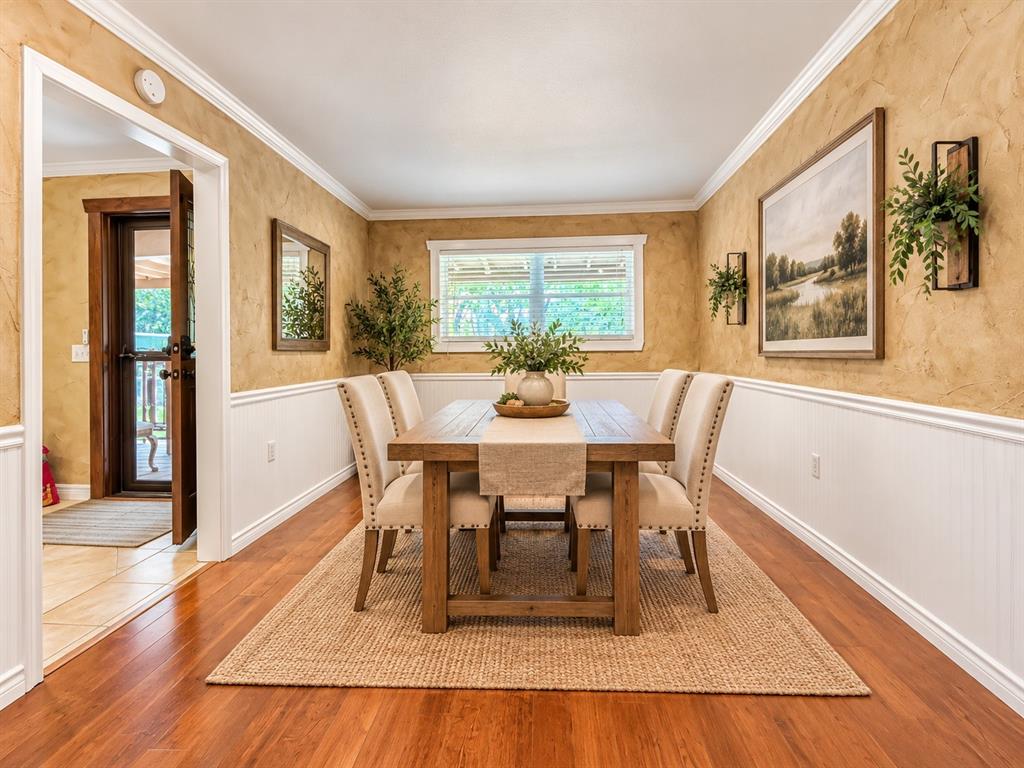 Dining room featuring wood-finish flooring, two-toned walls with beadboard wainscoting, crown molding, and a single-hung window Dining room featuring wood-finish flooring, two-toned walls with beadboard wainscoting, crown molding, and a single-hung window