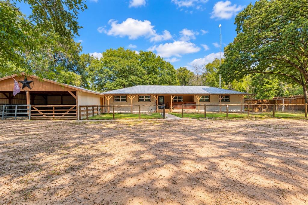 Exterior featuring a light-toned facade, metal roof, covered front porch with wooden support beams, and attached carport with post-and-rail fencing Exterior featuring a light-toned facade, metal roof, covered front porch with wooden support beams, and attached carport with post-and-rail fencing