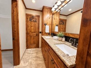 Bathroom featuring custom wood cabinetry, stone-finish countertop with an integrated rectangular sink, stone-tile flooring, and a large wood-framed mirror Bathroom featuring custom wood cabinetry, stone-finish countertop with an integrated rectangular sink, stone-tile flooring, and a large wood-framed mirror