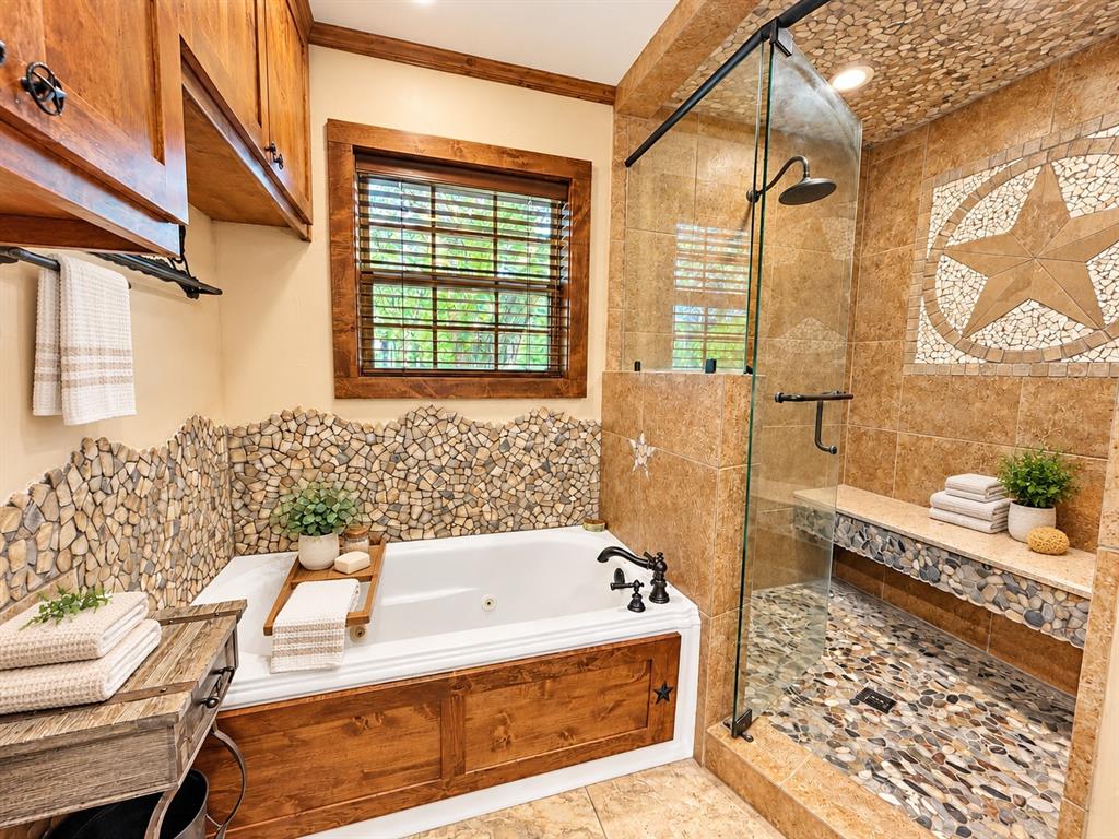 Soaking tub with custom wood paneling and stone tile surround, walk-in shower featuring pebble tile flooring, built-in stone bench, glass enclosure, and oil-rubbed bronze hardware Soaking tub with custom wood paneling and stone tile surround, walk-in shower featuring pebble tile flooring, built-in stone bench, glass enclosure, and oil-rubbed bronze hardware