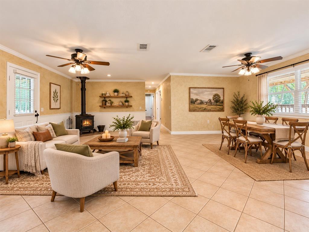 Open-concept living and dining area featuring ceramic tile flooring, a freestanding wood-burning stove, dual ceiling fans, and built-in wall shelving Open-concept living and dining area featuring ceramic tile flooring, a freestanding wood-burning stove, dual ceiling fans, and built-in wall shelving