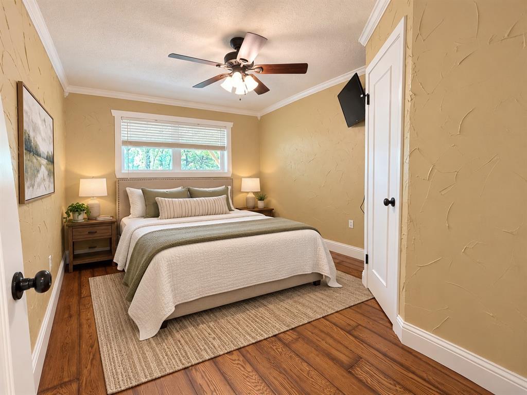 Wood-finish flooring, textured wall finishes, crown molding, a single-hung window with blinds, and a central ceiling fan with integrated lighting