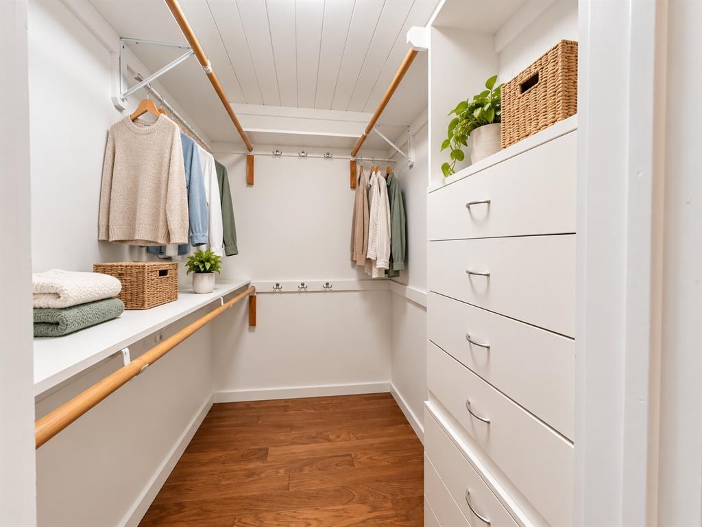Walk-in closet featuring built-in white drawer storage, wood-finish flooring, dual-level wooden hanging rods, wall-mounted metal hardware hooks, and white plank-style ceiling detailing
