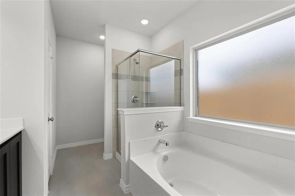 Bathroom featuring a deep soaking tub, separate glass-enclosed shower with tile surround, frosted privacy window, and recessed ceiling lighting