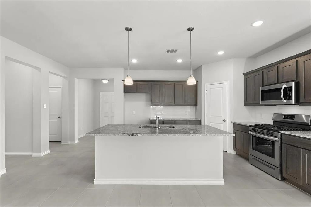 Kitchen featuring a center island with stone-finish countertops, dark wood cabinetry, stainless steel appliances, and dual pendant lighting