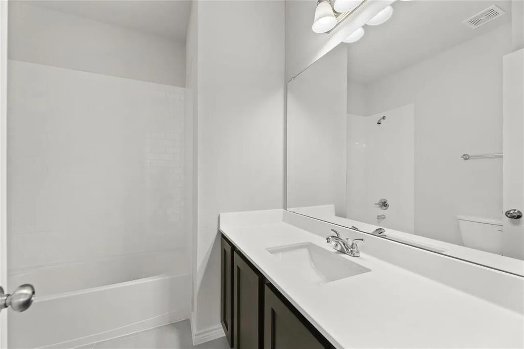 Bathroom #2 featuring a vanity with a white countertop and rectangular undermount sink, dark-toned cabinetry, a full-width wall mirror, and a tub-shower combination with a surround