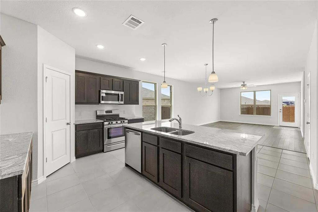 Kitchen featuring dark cabinetry, stone-surface countertops, stainless steel appliances, a central island with an integrated sink, and tile flooring