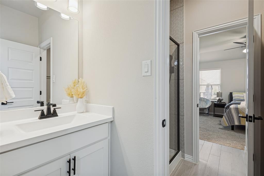 Bathroom vanity with solid surface countertop, rectangular under-mount sink, and matte black hardware, accompanied by a shower featuring herringbone-patterned tile and a glass enclosure