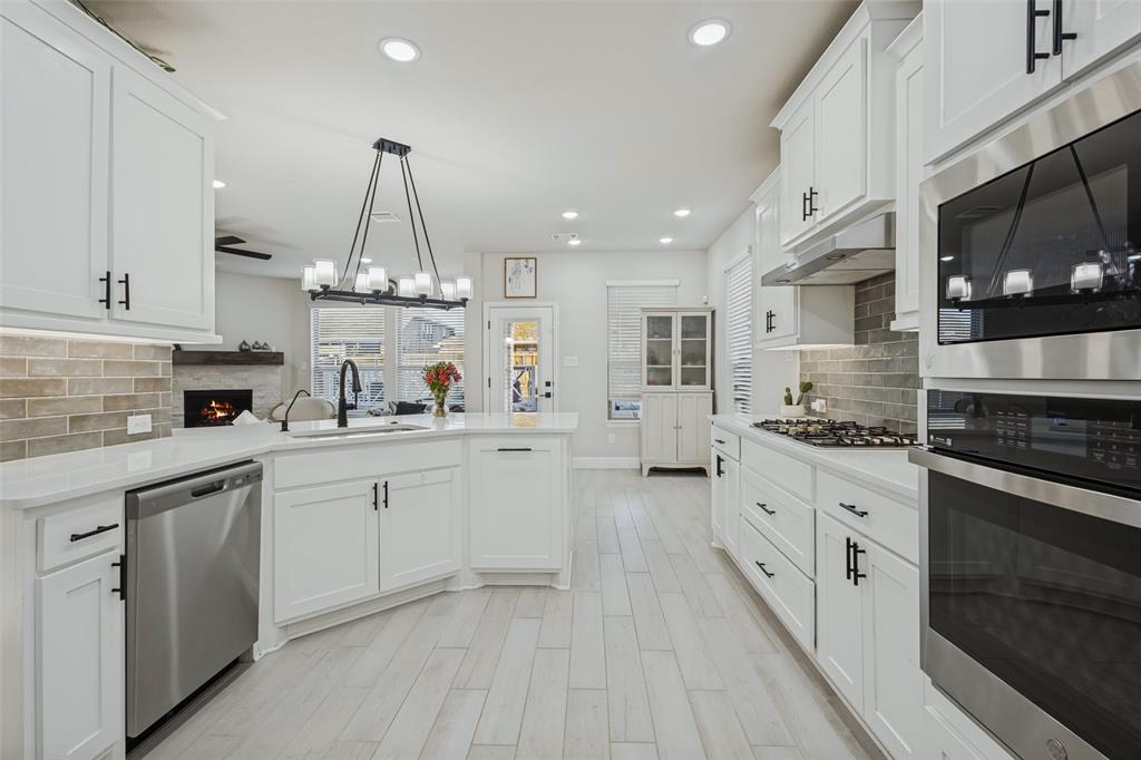Kitchen featuring white shaker-style cabinetry, stainless steel appliances, a multi-light linear pendant fixture, subway tile backsplash, and light-toned wood-finish flooring