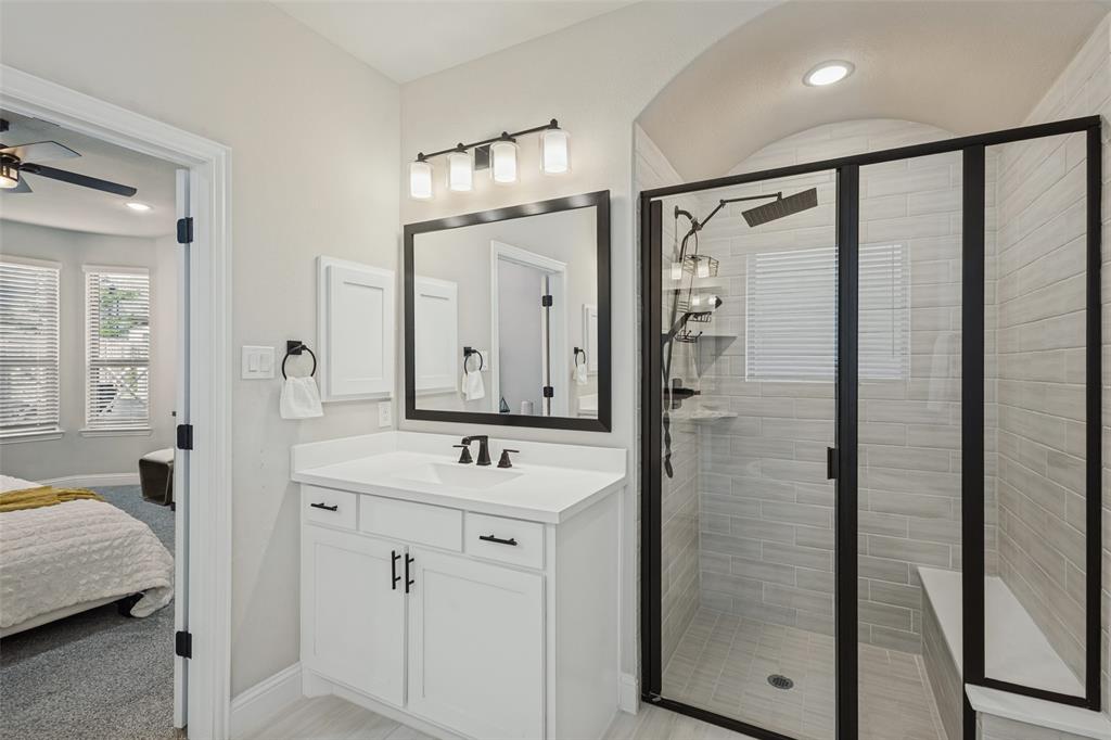 Bathroom featuring a vanity with a rectangular sink, black-finish hardware, a framed mirror, a four-light fixture, and a tiled shower stall with a built-in bench and glass enclosure