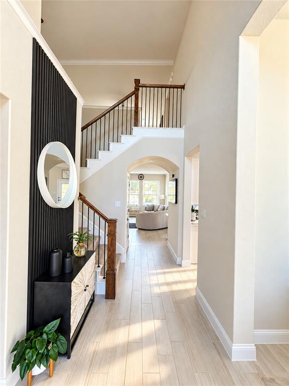 Foyer featuring vertical slat wall detailing, wood-finish flooring, and a staircase with a wooden handrail and metal balusters under a decorative archway