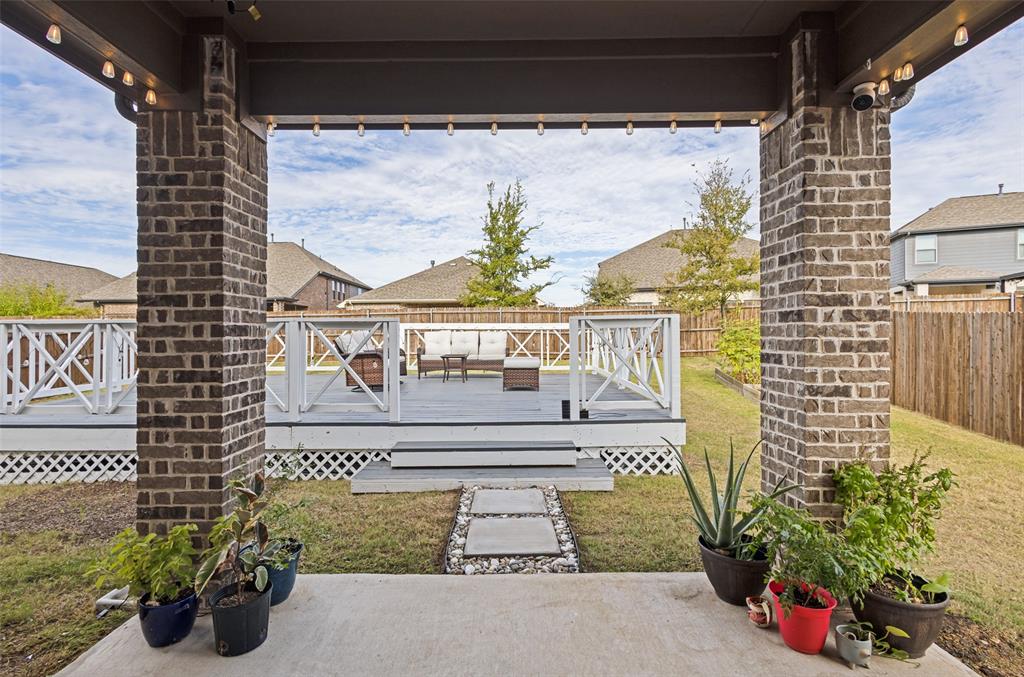 Covered patio featuring brick support columns, multi-level wood-finish decking, and white lattice railing