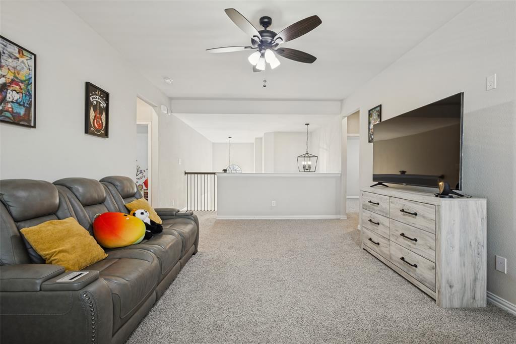 Neutral-toned interior space featuring a ceiling fan with integrated lighting, neutral wall-to-wall carpeting, and a metal stair railing