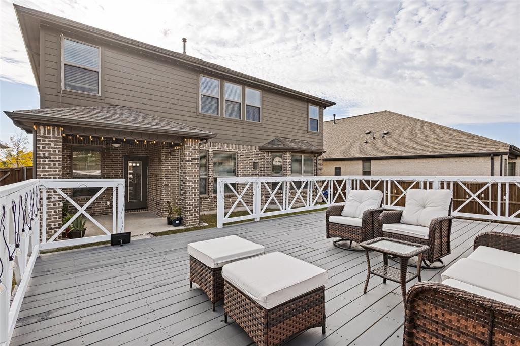 Expansive elevated deck featuring composite wood-finish decking and white cross-buck railing, complemented by a covered patio with brick pillars and horizontal siding exterior