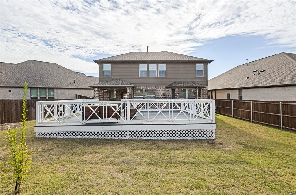 Raised wooden deck featuring decorative white X-pattern railing and white lattice skirting, complemented by a fenced backyard