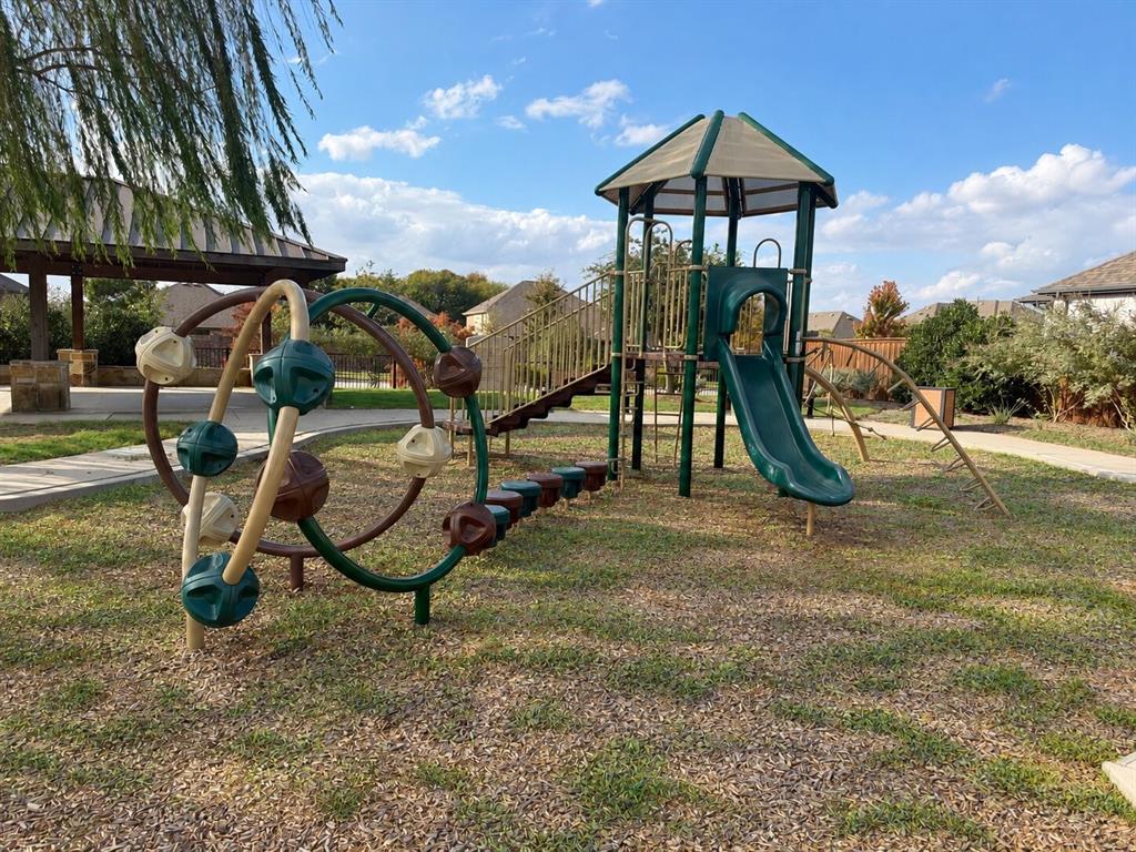 Outdoor recreation area featuring a multi-level playground structure with a slide and climbing equipment, situated on a mulched surface with an attached pavilion