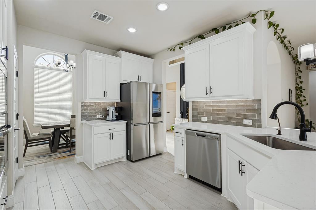 Kitchen featuring white cabinetry, light-toned stone-finish countertops, linear tile backsplash, stainless steel appliances, and wood-finish flooring