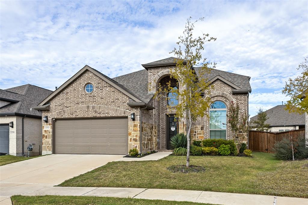 Multi-gable brick and stone exterior featuring an arched entryway, decorative oculus window, and attached two-car garage