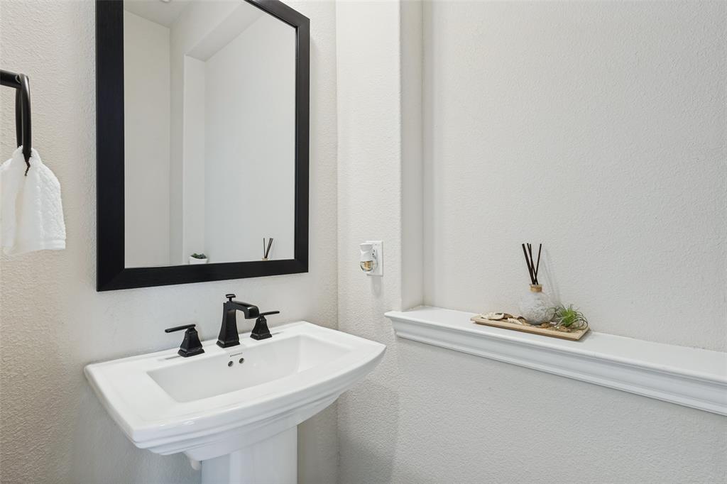 Pedestal sink featuring a wide basin and widespread matte black faucet, paired with a framed rectangular wall mirror