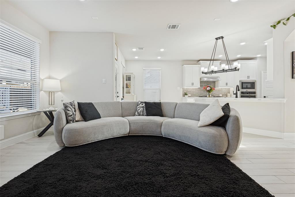 Open-concept living space featuring wood-finish tile flooring, recessed lighting, white shaker-style cabinetry, a stone-tiled backsplash, and a multi-light linear chandelier