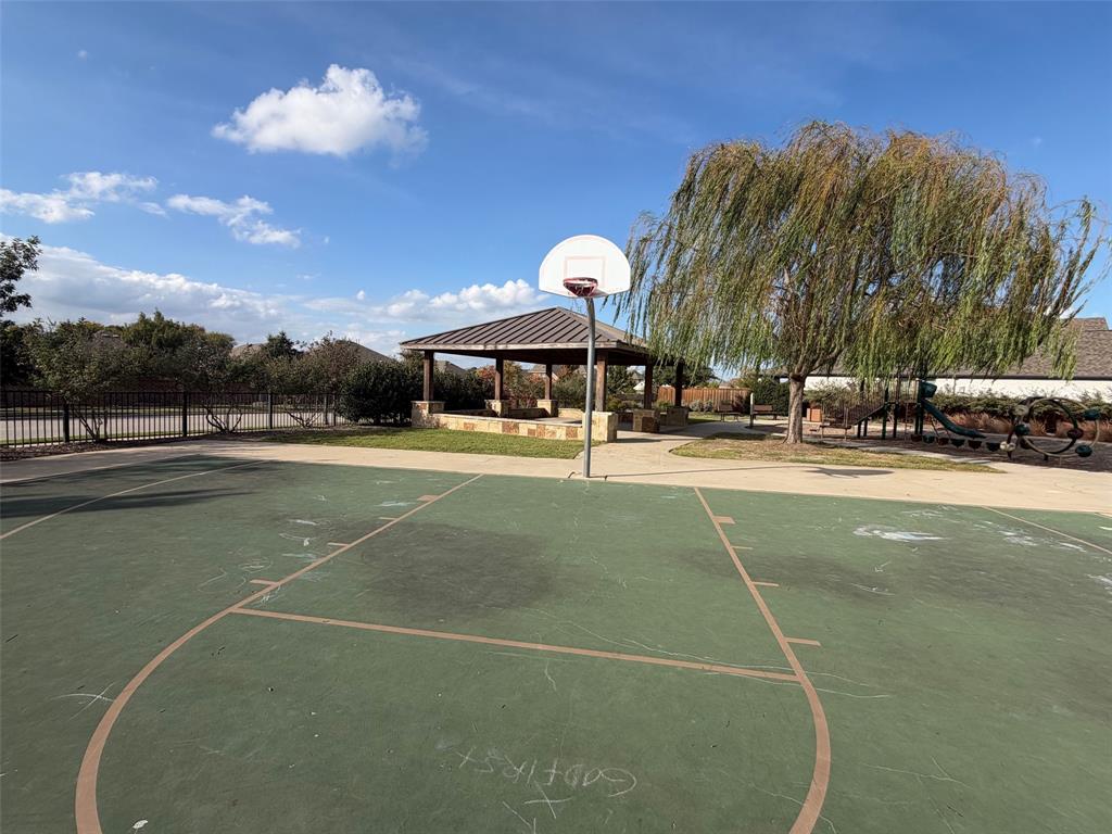 Outdoor recreation area featuring a paved basketball court, a covered stone pavilion, and mature willow trees