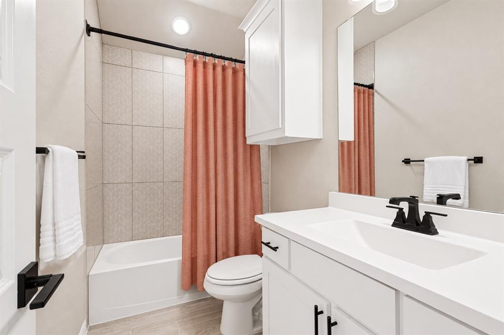 Bathroom featuring a white vanity cabinet, solid-surface countertop with integrated sink, matte black hardware, wall-mounted medicine cabinet, and a tiled tub-shower surround