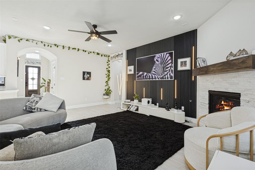 Living area featuring a vertical slat accent wall with integrated lighting, a stone-surround fireplace with a timber mantel, recessed ceiling lights, and a ceiling fan
