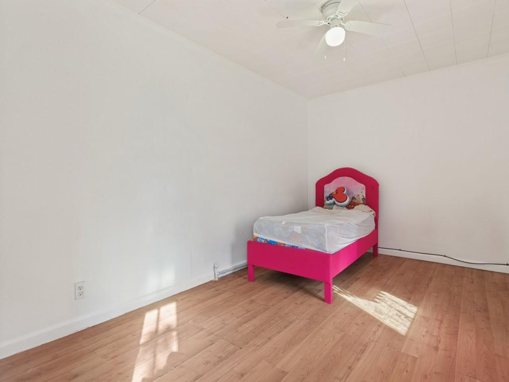 Neutral interior space featuring wood-finish flooring, white walls, and a ceiling-mounted light fixture with integrated fan
