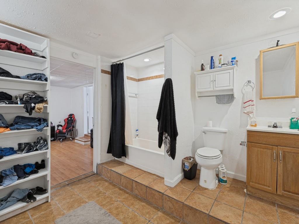 Bathroom featuring ceramic tile flooring, a raised tub surround, a wood-finish vanity with a built-in medicine cabinet, and integrated shelving