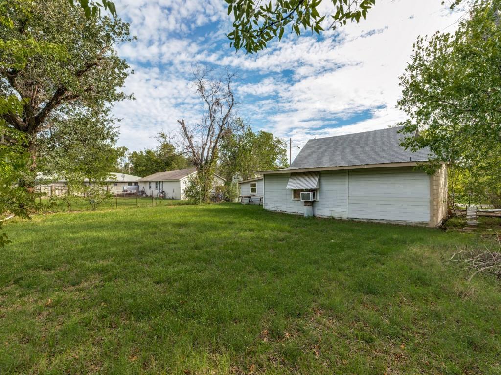 Expansive backyard featuring a large grass lawn, mature trees, and a detached outbuilding with a metal awning