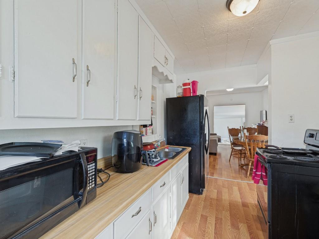 Kitchen featuring white cabinetry with silver-tone hardware, wood-finish countertops, wood-finish flooring, and a ceiling-mounted light fixture
