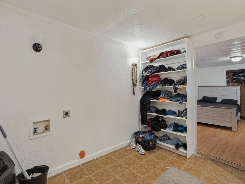 Utility area featuring wall-mounted light fixtures, built-in open shelving, and integrated washer and dryer hookups with tile flooring
