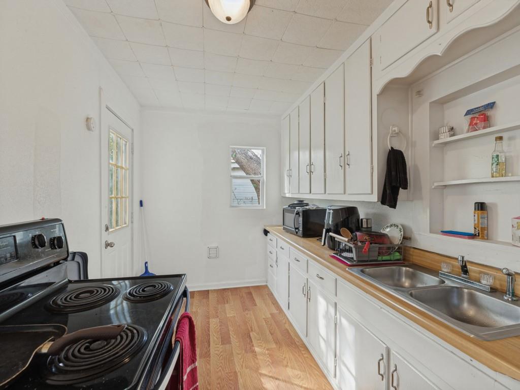 Kitchen featuring wood-finish flooring, white cabinetry with integrated shelving, dual-basin stainless steel sink, and a glass-paneled exterior door