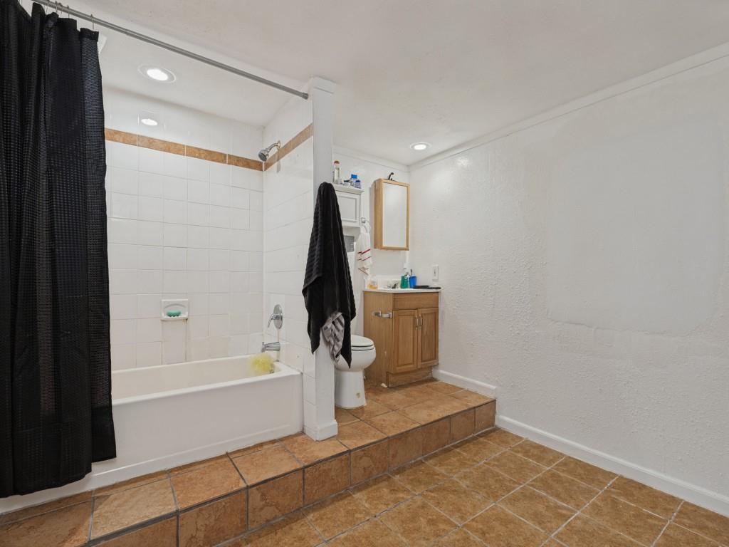 Bathroom featuring a raised platform floor with ceramic tile, a shower-tub combination with white wall tile, a wooden vanity cabinet, and recessed ceiling lighting
