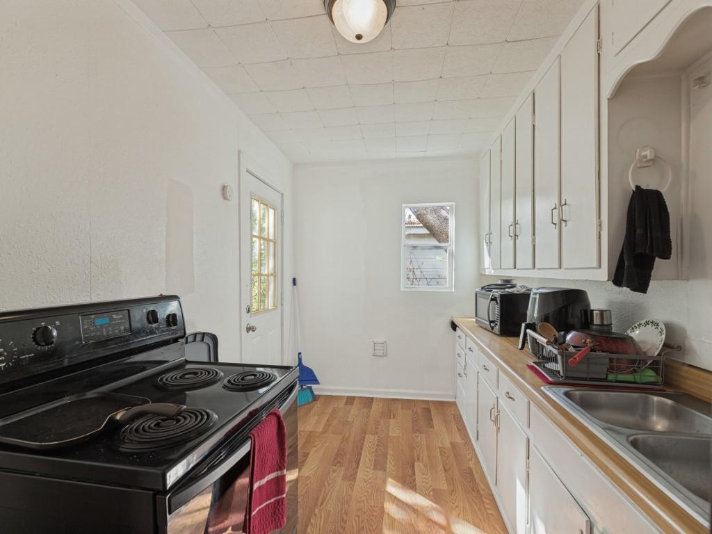 Kitchen featuring white cabinetry, wood-finish flooring, a double-basin stainless steel sink, and a black electric range