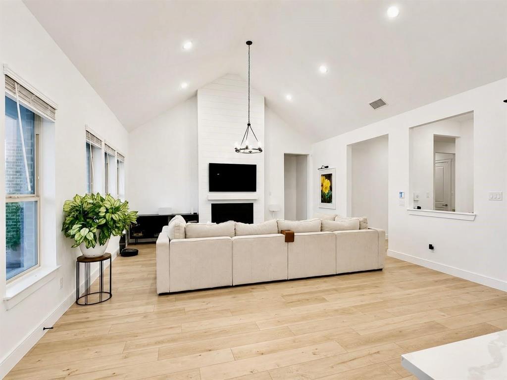 Vaulted ceilings, wood-finish flooring, recessed lighting, and a floor-to-ceiling fireplace with a prominent mantel Vaulted ceilings, wood-finish flooring, recessed lighting, and a floor-to-ceiling fireplace with a prominent mantel