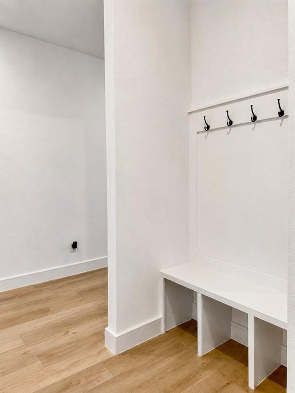 Built-in storage bench featuring white millwork, integrated coat hooks, and wood-finish flooring Built-in storage bench featuring white millwork, integrated coat hooks, and wood-finish flooring