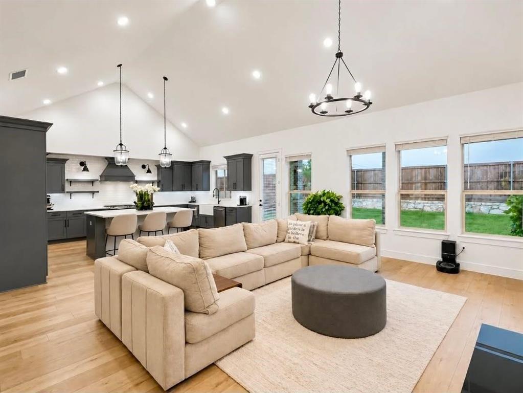 Vaulted ceilings with recessed lighting, wood-finish flooring, kitchen island with breakfast bar, dark-toned cabinetry, and a tiered chandelier Vaulted ceilings with recessed lighting, wood-finish flooring, kitchen island with breakfast bar, dark-toned cabinetry, and a tiered chandelier