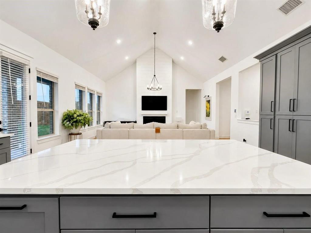 Expansive kitchen island with a white quartz countertop, floor-to-ceiling gray cabinetry, vaulted ceilings, and a fireplace with shiplap detailing Expansive kitchen island with a white quartz countertop, floor-to-ceiling gray cabinetry, vaulted ceilings, and a fireplace with shiplap detailing